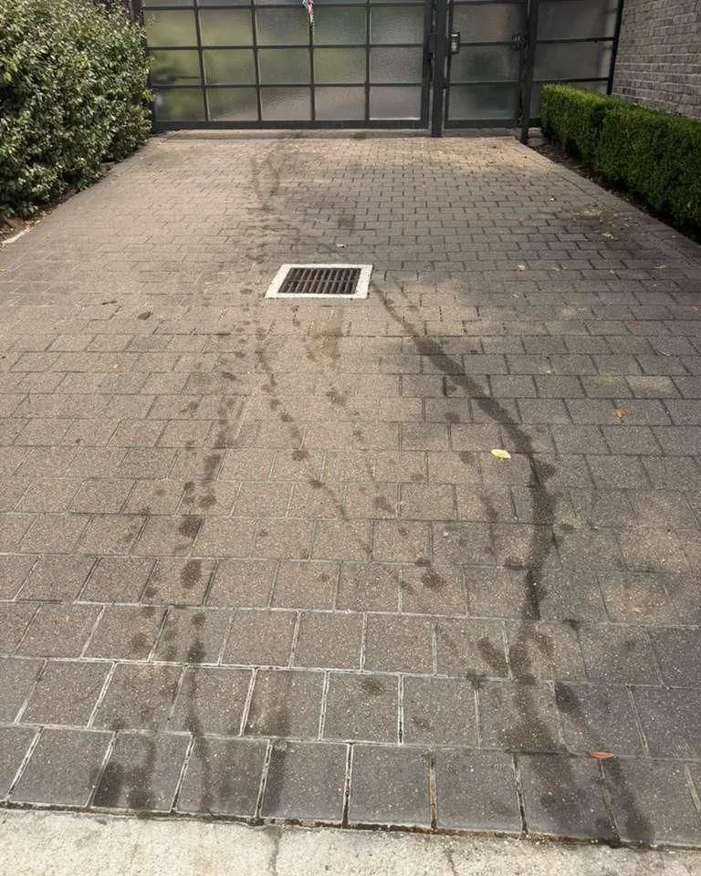 Before: twin hydraulic fluid streaks on pavers at the drain in front of a driveway gate