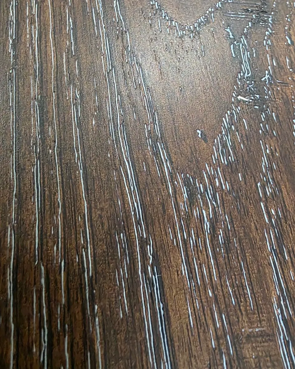 Before: drywall joint compound filling the grain of textured LVP flooring after a fire rebuild in Houston