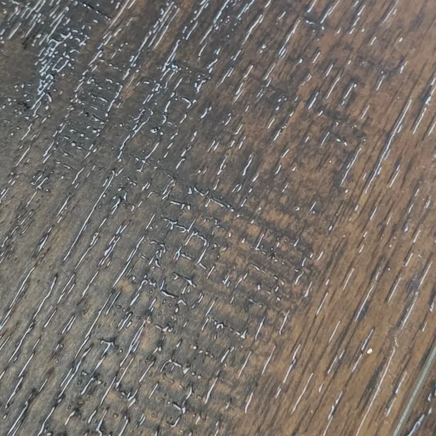Close-up of drywall joint compound packed into the embossed wood-grain texture of luxury vinyl plank, with the trowel pattern visible