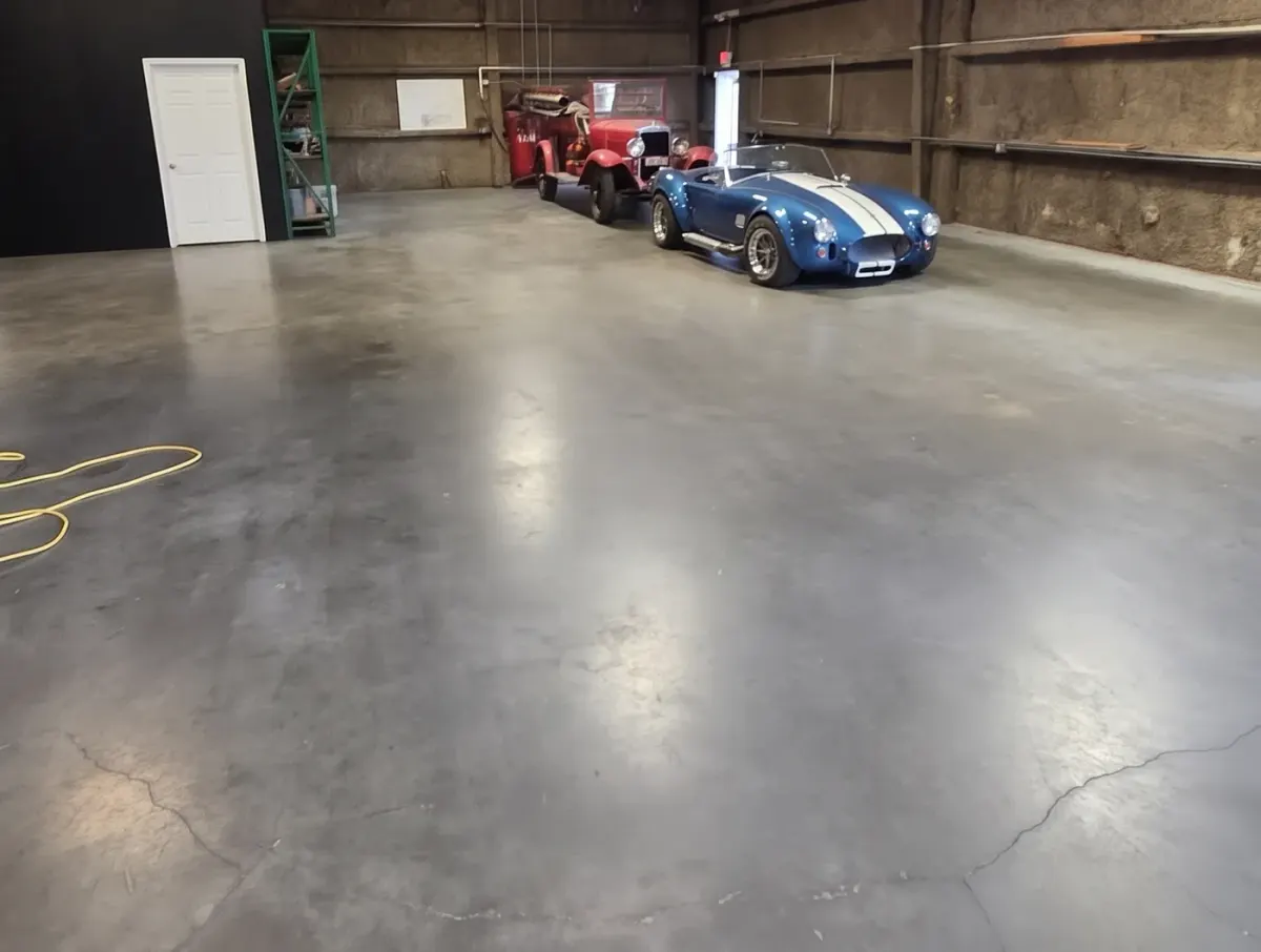Bare concrete shop floor in Houston after a first machine scrub by Maddox Surface, with the owner’s vehicles at the far wall